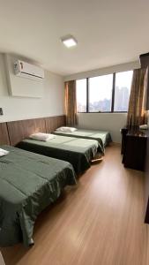 a room with three beds and a large window at Hotel Itamaraty in Curitiba