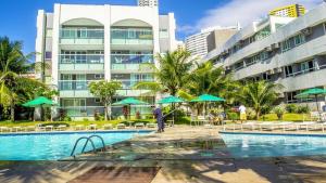 a resort pool with tables and umbrellas in front of a building at Beira a mar Ponta Negra Beach, Lovely Flat Natal RN in Natal