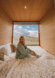 a woman sitting on a bed looking out a window at Nomads Ecuador in Chimborazo