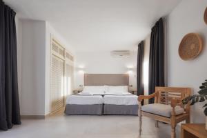 a white bedroom with a bed and a chair at Alojamientos Turísticos Cardona - Estudio Doble Superior in Es Pujols
