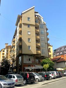 a tall building with cars parked in a parking lot at KENT Apartments in Pristina