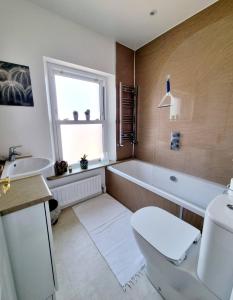 a bathroom with a tub and a toilet and a sink at Cosy Family Haven: Spacious 3-Bedroom Retreat in Christchurch in Iford