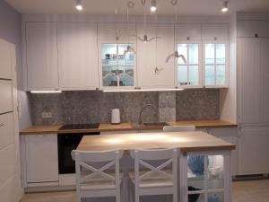 a kitchen with white cabinets and a table and stools at WYSPA MEW - apartament PREMIUM z prywatnym ogrodem, 150 m od plaży in Gąski