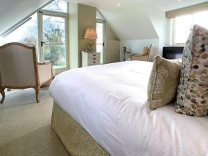 a bedroom with a white bed with a chair and windows at The Gatehouse - UK36939 in Lamerton