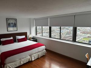 a bedroom with a large bed with red sheets and windows at Hotel Oceanía Bogotá Museo in Bogotá