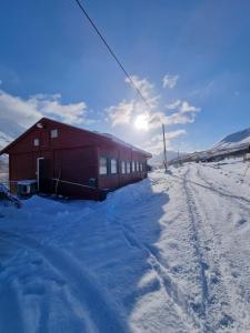 a red building in the snow with the sun behind it at Storgalten gjestehus in Nord-Lenangen