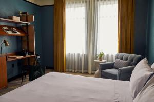 a bedroom with a bed and a chair and window at Hotel Emeline in Charleston