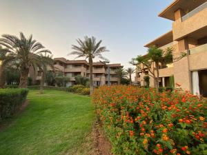 an apartment complex with palm trees and a field of flowers at Corail Apart Golfique -Prestigia in Marrakech