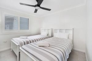 two beds in a white room with a ceiling fan at Amaroo in Gerroa