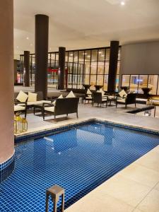 a swimming pool in a hotel lobby with chairs and tables at StaySuites The Apple Melaka in Malacca