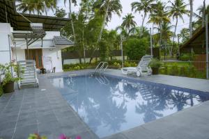 a swimming pool with two lawn chairs and palm trees at Waves and Shores Pool Beach Villa in Mararikulam