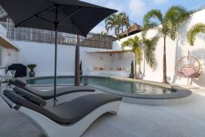 a swimming pool with lounge chairs and an umbrella at Villa Weiss Berawa in Canggu