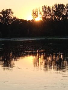 einen Sonnenuntergang über einem Wasserkörper mit Bäumen in der Unterkunft Suite avec SPA et SAUNA privatif in Vallères