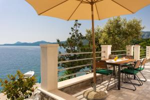 a table with an umbrella on a balcony next to the water at Apartments Laurea in Slano