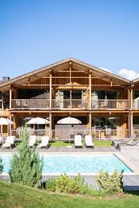 un grand bâtiment avec une piscine, des chaises et des parasols dans l'établissement Dolmites Nature Hotel Vigilerhof, à Alpe di Siusi