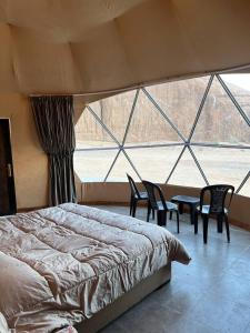 una camera da letto con un letto e sedie e una grande finestra di Wild Oryx Camp Bubbles a Wadi Rum