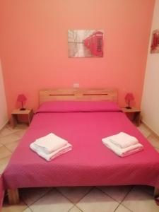 1 dormitorio con 1 cama rosa y 2 toallas en B&B Bella Calasetta, en Calasetta
