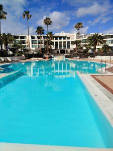 a large blue swimming pool with a hotel in the background at Bungalow La Palmera - 2 bedroom - PLAYA ROCA residence sea front access - Pool View - Free AC - Wifi in Costa Teguise