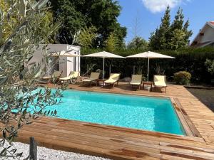 una piscina con sedie e ombrelloni su una terrazza di legno di Hôtel Le Grain de Sable ad Arès