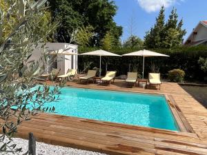 a pool with chairs and umbrellas on a wooden deck at Hôtel Le Grain de Sable in Arès