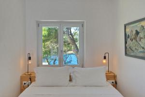 a bedroom with a bed with white sheets and a window at Kavos Villa in Aghios Petros Alonissos