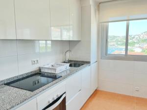 a white kitchen with a sink and a window at Ático Pampaído in Raxó +2 photos