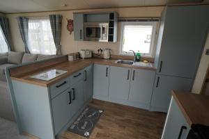 una pequeña cocina con armarios blancos y fregadero en Heacham Sunset lodge Platinum van, en Hunstanton