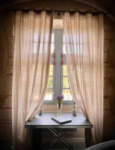 a window with curtains and a table with flowers on it at Au pays de Gide appart feutré dans un château in Lussan