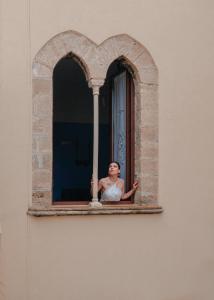 une femme regarde par une fenêtre dans l'établissement La Bifora e il granaio, à Sciacca
