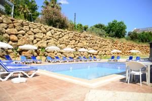 a pool with chairs and umbrellas next to a stone wall at Lofts Alanya Lina in Okurcalar
