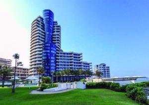 a tall blue building with a park in front of it at Pearls of Umhlanga Multi-Story Penthouse in Durban