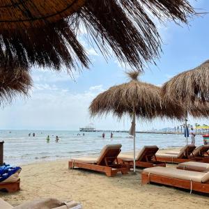 ein Strand mit Stühlen und Sonnenschirmen und Menschen im Wasser in der Unterkunft Hotel Vila MAX in Durrës