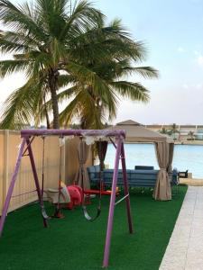 eine Schaukel am Strand mit einer Palme in der Unterkunft درة العروس فيلا البيلسان الشاطي الازرق in Durrat Al-Arus