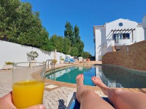 a person holding a glass of orange juice next to a swimming pool at Casa Luna, Burgau - Luz, Lagos in Burgau