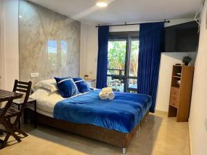1 dormitorio con cama con sábanas azules y ventana en Ahuzat Shaul Hotel Seaside en H̱adera