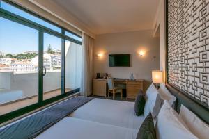 a bedroom with a bed with a large window and a desk at Hotel Mundial in Lisbon