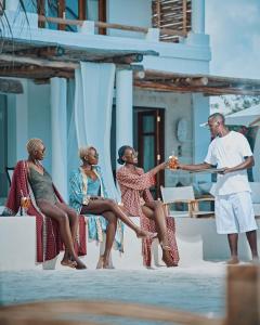 a group of four women sitting on a ledge with a man holding a drink at Simba Wa Kale Suites & Beach in Watamu