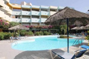 a swimming pool with chairs and an umbrella and a hotel at Apartamento con piscina climatizada y vista al mar in San Bartolomé de Tirajana