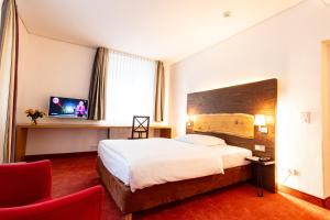 Cette chambre d'hôtel comprend un grand lit et un fauteuil rouge. dans l'établissement Parkhotel Wolfsburg, à Wolfsburg