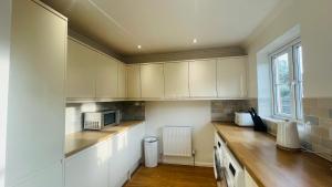 a kitchen with white cabinets and a microwave at Hana Holiday Home - 4 En-suite Bedroom house in Menai Bridge