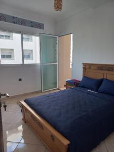 Schlafzimmer mit einem Bett mit blauer Bettwäsche und Fenstern in der Unterkunft Rawan Appart in Tangier