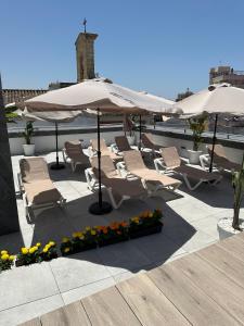 a patio with lounge chairs and umbrellas on a roof at esZentrico Suites Jerez in Jerez de la Frontera