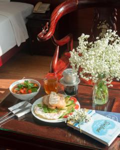 een tafel met een bord eten en een vaas met bloemen bij LE SOLEIL HOTEL managed by NEST Group in Nha Trang