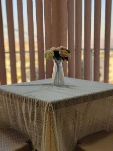 un jarrón blanco con flores sentado en una mesa en atoom lodge, en Jerash