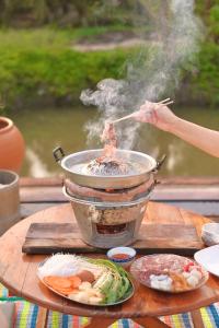 a person cooking food in a pot on a table at Lukmailhontaiton (ลูกไม้หล่นใต้ต้น) 