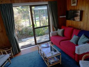 a living room with a red couch and a large window at Theo's Cottage in Waikanae