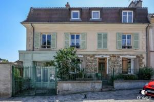 a large stone house with green windows and a gate at L' Eglise - 2 pièces avec balcon au dernier étage vue Paris in Saint-Prix
