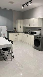 una cocina con armarios blancos, mesa y electrodomésticos en dana hotel apartments en Taif
