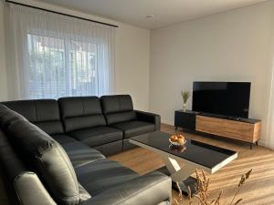 sala de estar con sofá de cuero negro y TV en Villa BEBRŲ NAMAI with Hot Tub, en Ginduliai