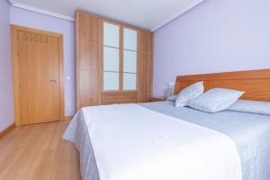 a bedroom with a white bed and a wooden door at Apartamento Subráu in Gijón